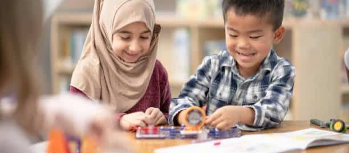 A Muslim girl and an Asian boy is doing crafts together at their public library.